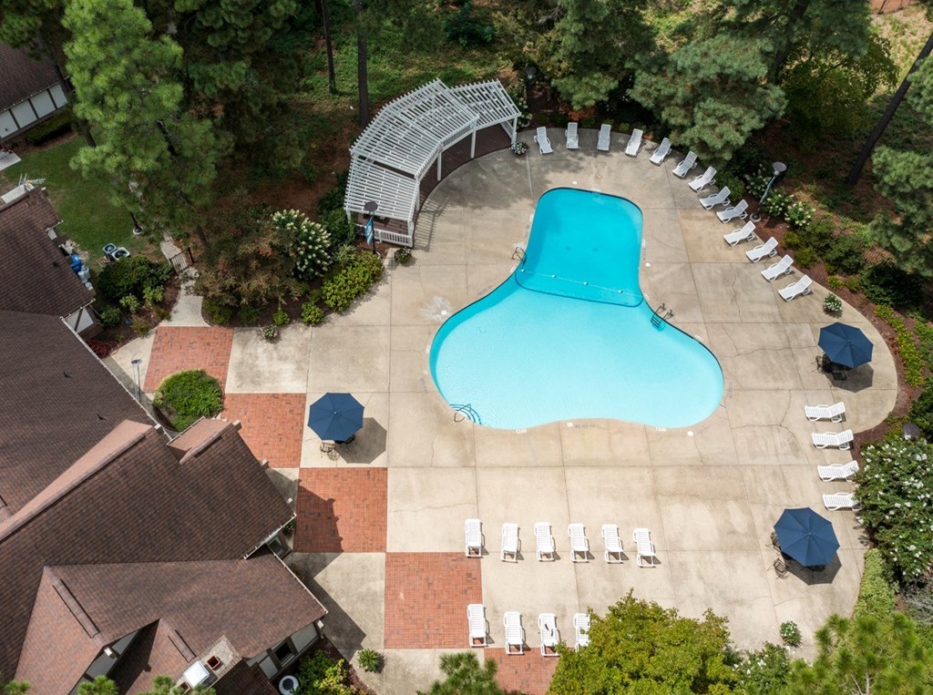 A large blue kidney-shaped pool surrounded by white lounge chairs and umbrellas.