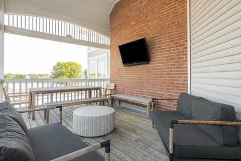 A balcony with a grey couch, a white ottoman and a flat screen TV mounted on a brick wall. at Sundance Apartments, Indianapolis, IN