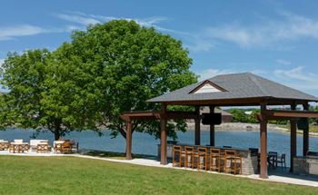 A gazebo with a table and chairs is situated on a lawn by a body of water