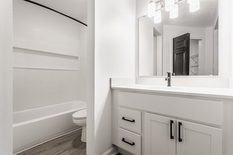 A white bathroom with a tub, sink, and mirror. at Sundance Apartments, Indianapolis