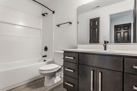 A white toilet sits in a bathroom with a wooden vanity and a large mirror. at Sundance Apartments, Indiana