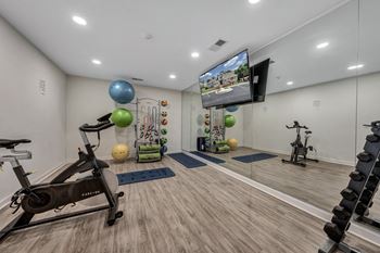 A home gym with a variety of exercise equipment including a stationary bike, a treadmill, and a television mounted on the wall. at Sunscape Apartments, Roanoke