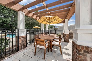 A wooden table and chairs are set up on a patio with a yellow umbrella. at Sunscape Apartments, Virginia