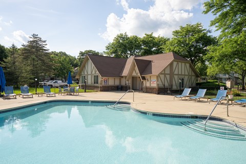 A swimming pool in front of a house with a deck and sun loungers.