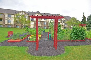 a garden with a pergola and benches in front of an apartment building at Tanglewood Apartments, Oak Creek, 53154