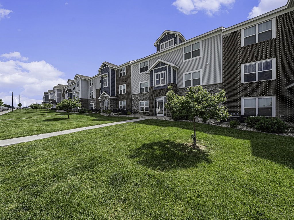 a green lawn with shade trees in front of an apartment building at Trade Winds Apartment Homes in Elkhorn, NE 68022