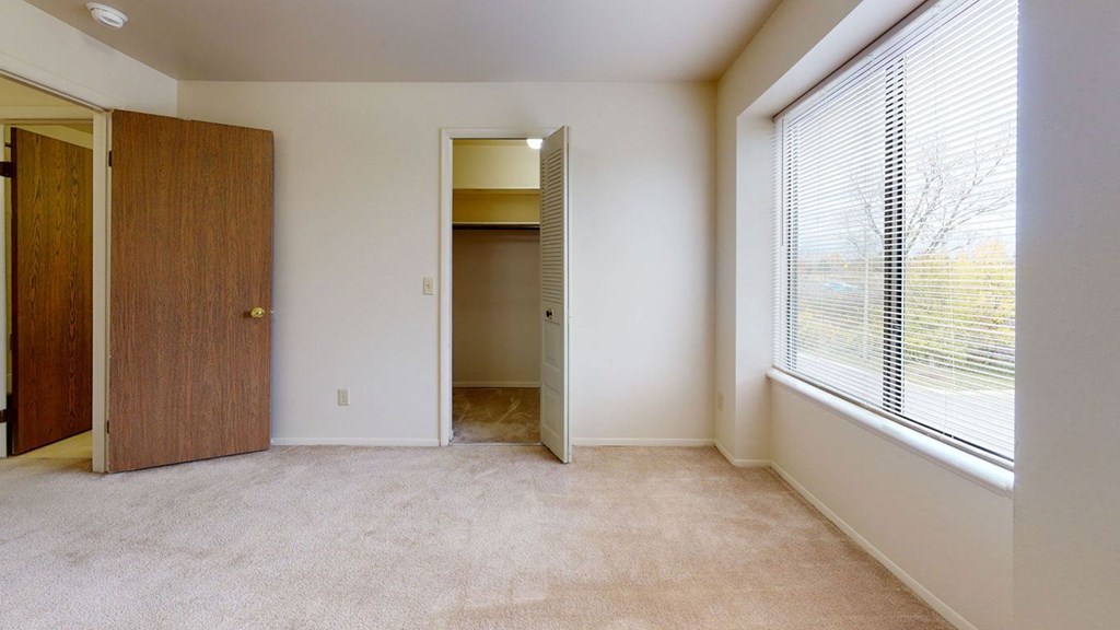 a bedroom with a large window and a door to a closet  at Trappers Cove Apartments, Michigan
