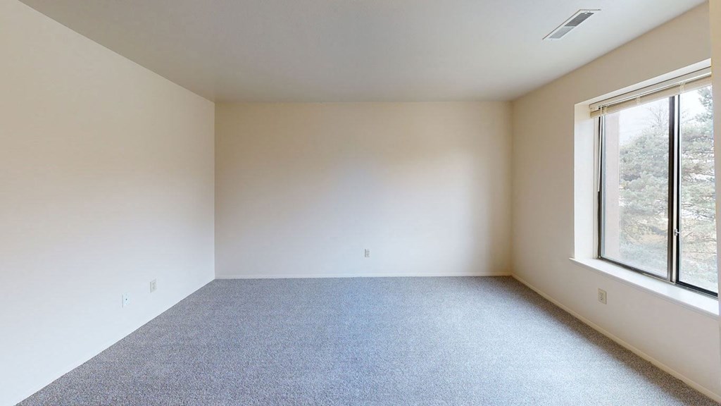 spacious bedroom with a large window and carpet  at Trappers Cove Apartments, Lansing