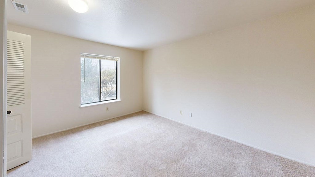 spacious bedroom with a large window and carpet at Trappers Cove Apartments, Michigan, 48910