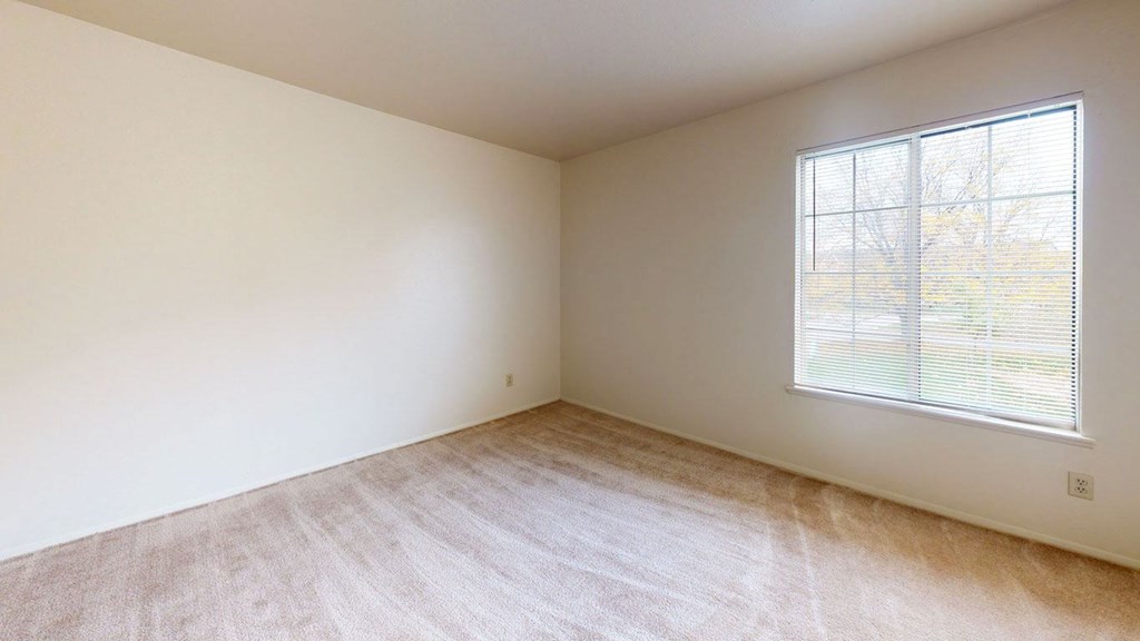 bedroom with a large window and plush carpeting  at Trappers Cove Apartments, Lansing, MI