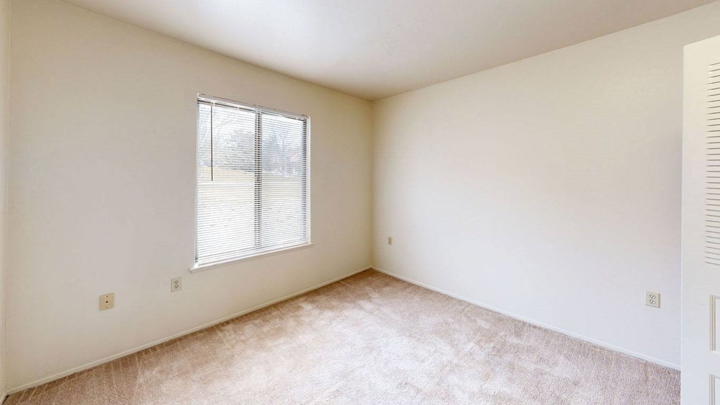 a bedroom with a window and a carpeted floor  at Trappers Cove Apartments, Lansing, 48910
