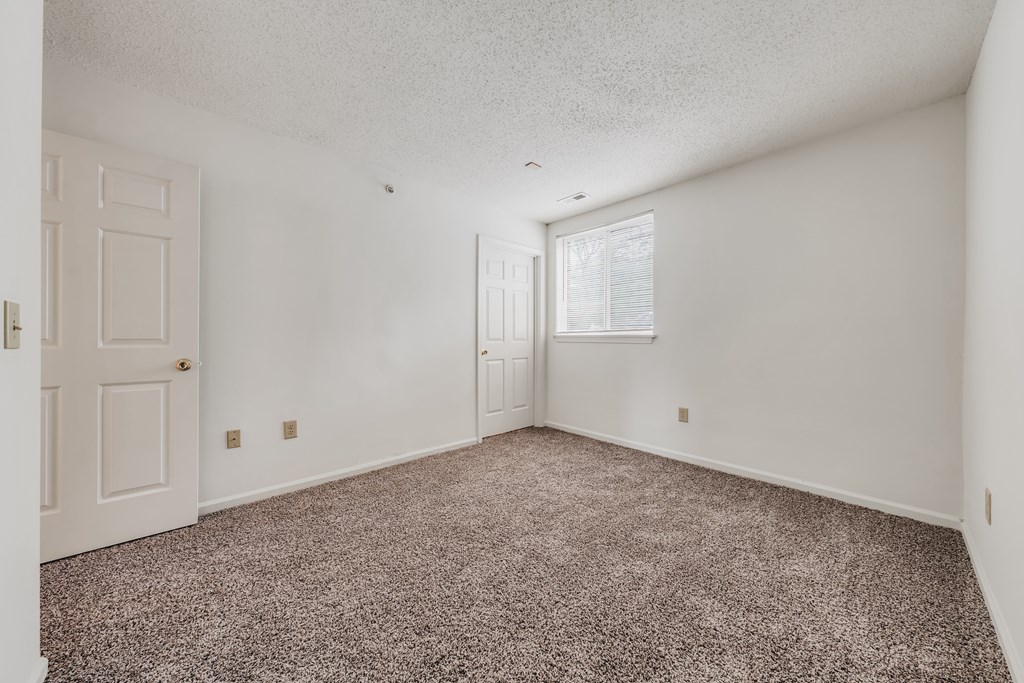 A room with a carpeted floor and a door on the left side at WaterFront Apartments, Virginia Beach, 23453