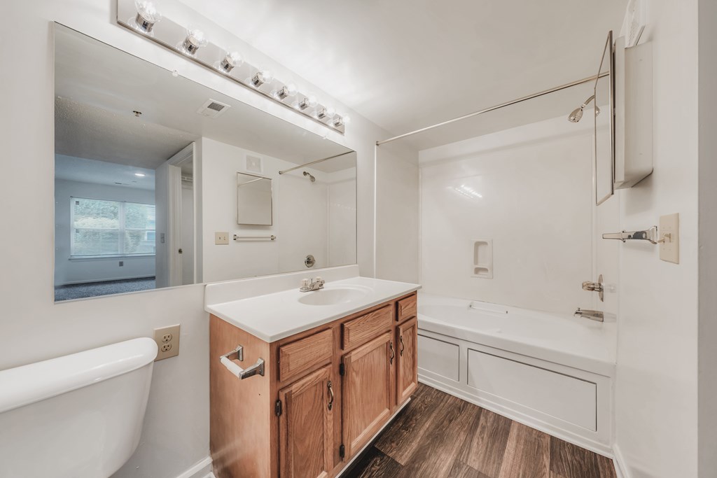 A white bathroom with a wooden vanity and a white bathtub at WaterFront Apartments, Virginia Beach, 23453