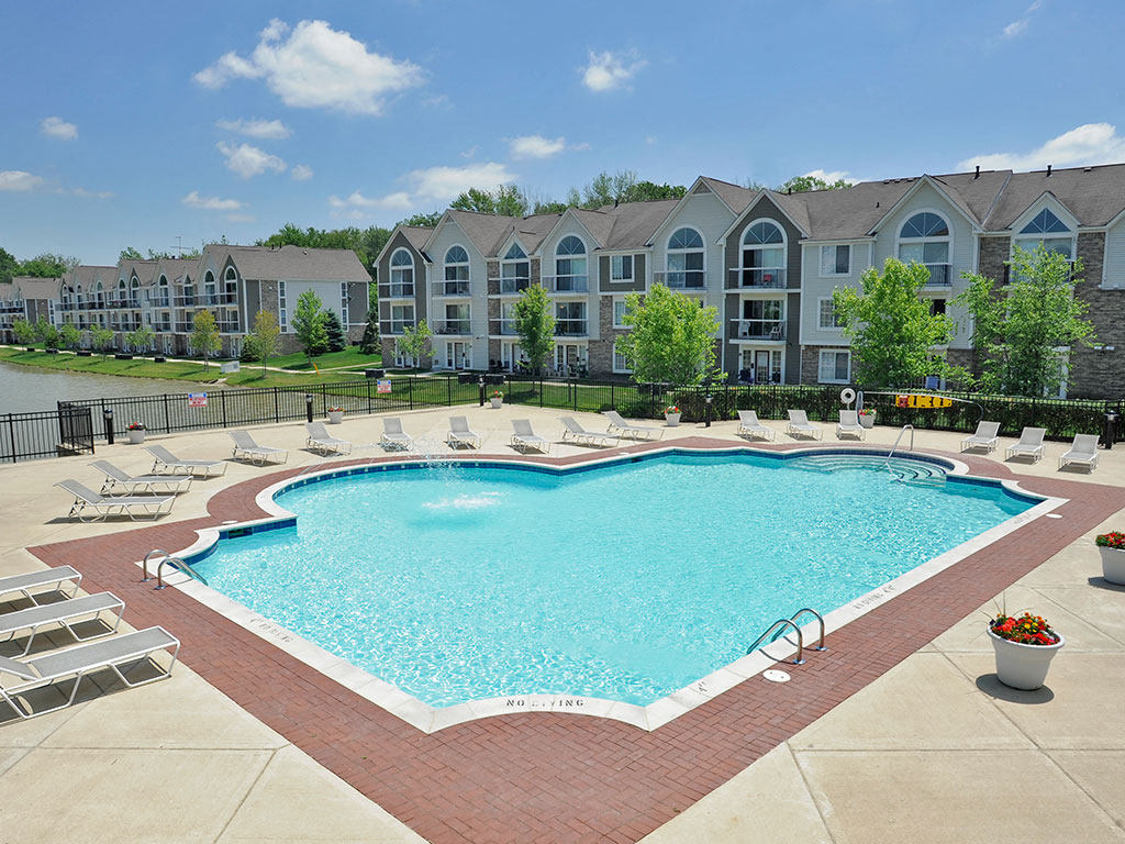 a swimming pool with lounge chairs around it in front of an apartment building