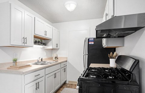 A black stove is in a white kitchen with a sink and cabinets.