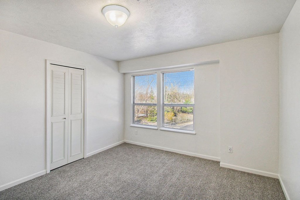 A bedroom with two windows and a door to a walk in closet at Brentwood Park Apartments, La Vista, Nebraska