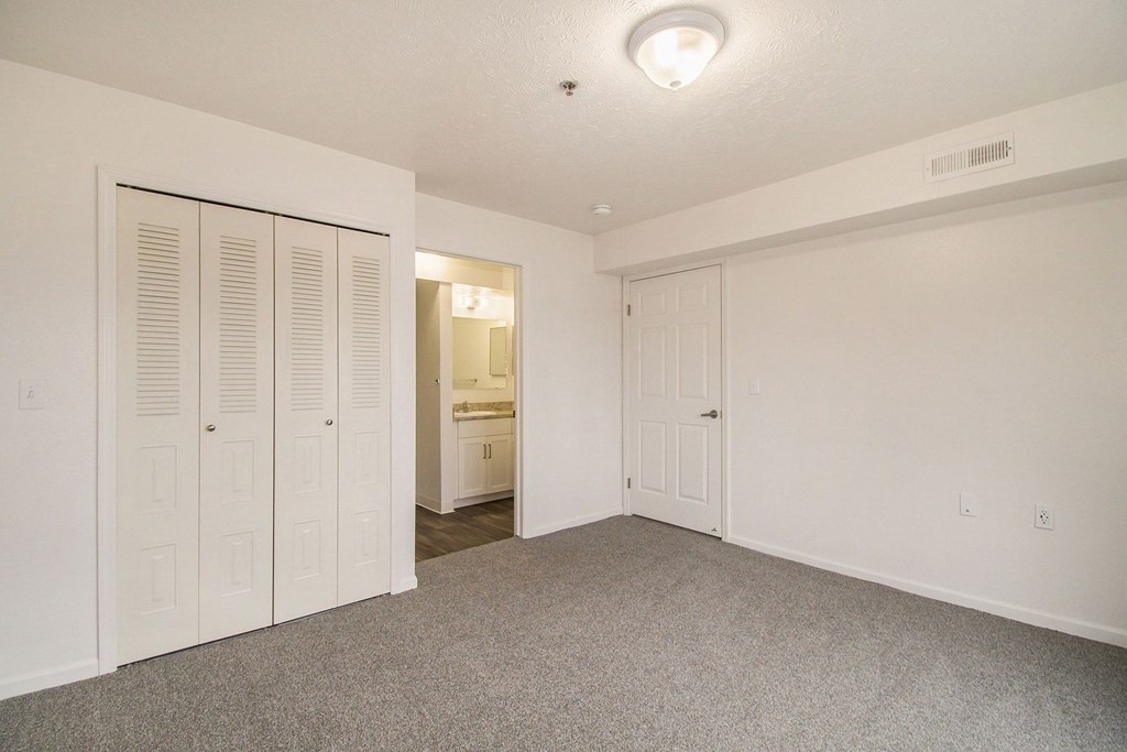 A bedroom with a carpeted floor and an ensuite and large closet at Brentwood Park Apartments, La Vista, Nebraska