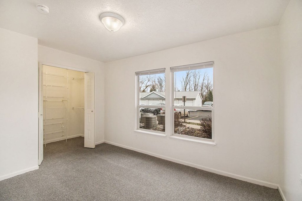 A bedroom with a carpeted floor, a walk in closet, and two windows at Brentwood Park Apartments, La Vista, Nebraska