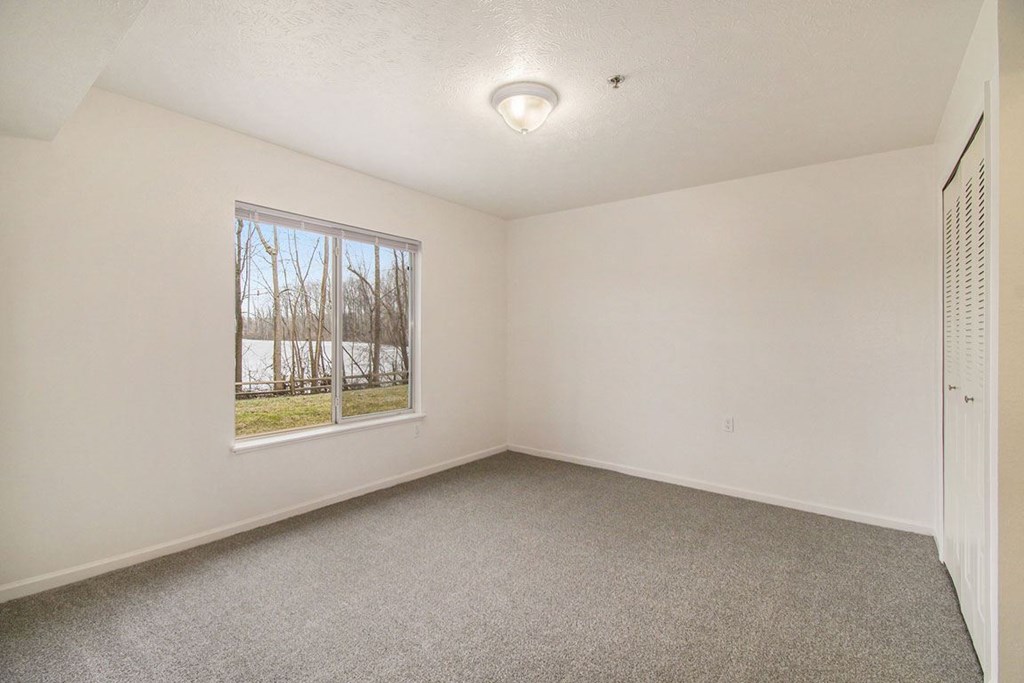 A bedroom with a window and a carpeted floor at Brentwood Park Apartments, La Vista, Nebraska