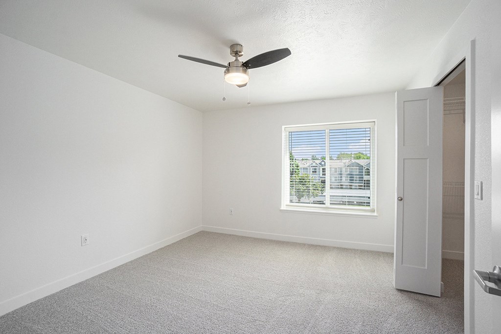 A bedroom with a ceiling fan and a window with blinds at Byron Lakes Apartments, Byron Center, Michigan