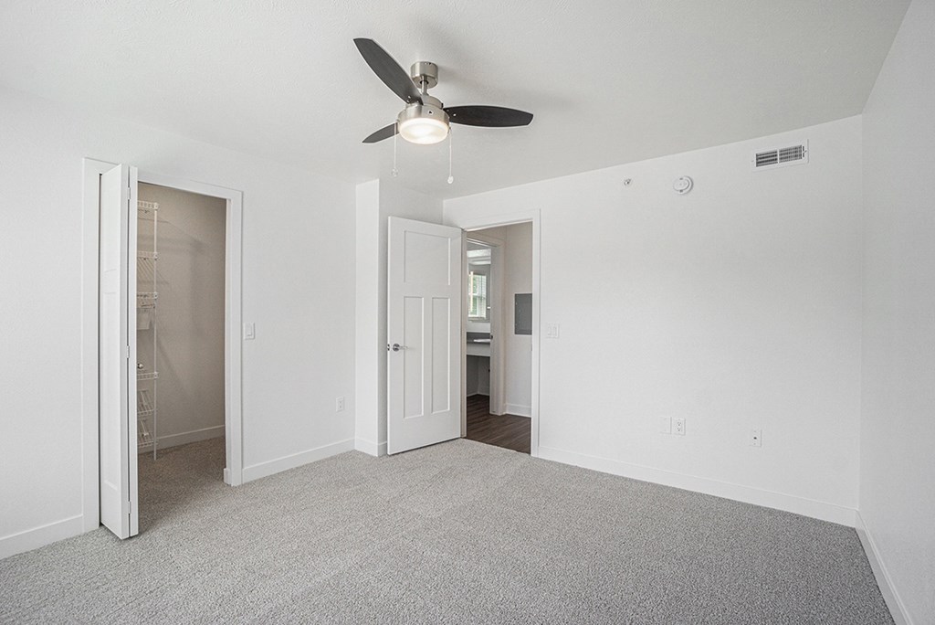 A bedroom with a ceiling fan, walk-in closet, and carpeted floor at Byron Lakes Apartments, Byron Center, Michigan