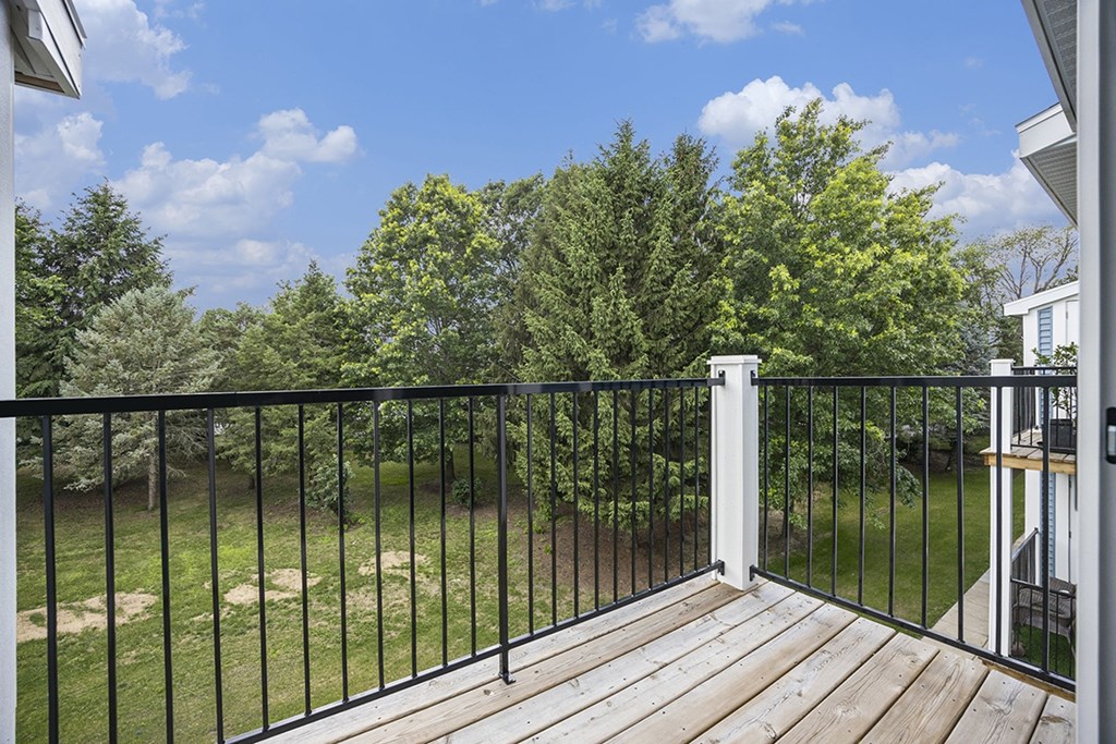 A balcony with a black railing overlooks a grassy area with trees at Byron Lakes Apartments, Byron Center, MI