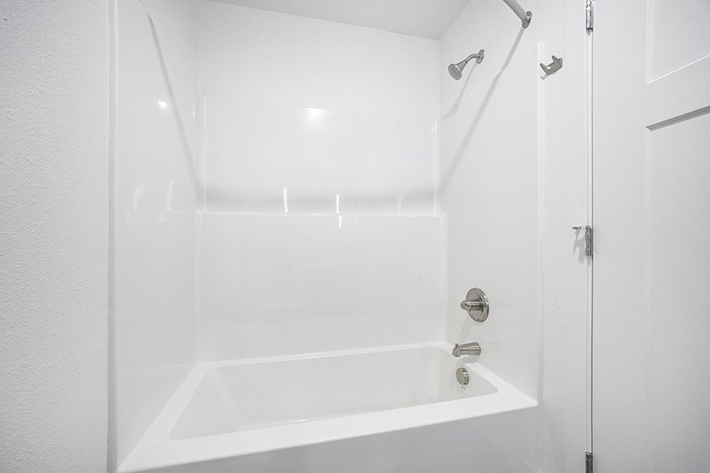 A white bathroom with a tub and shower at Byron Lakes Apartments, Byron Center, MI