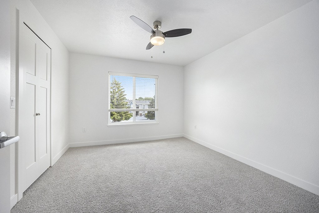 A bedroom with a ceiling fan and a window showing a view of trees at Byron Lakes Apartments, Byron Center, MI