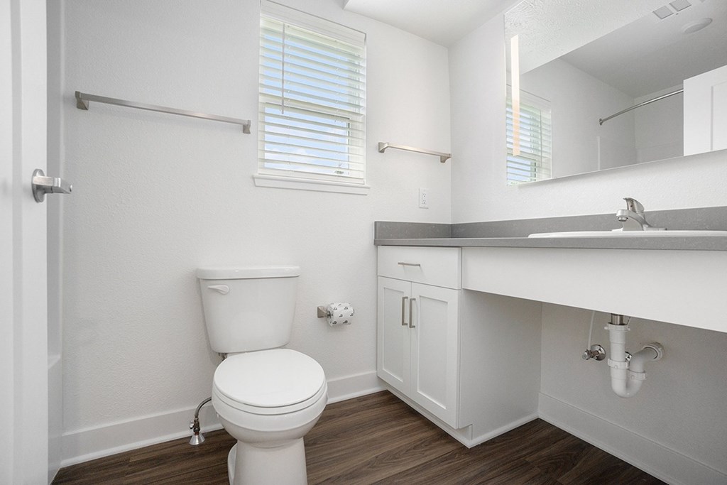 A bathroom with a window, toilet with a white cabinet and sink at Byron Lakes Apartments, Byron Center, Michigan