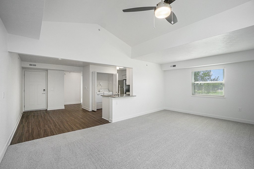 An enlarged living room with a cathedral ceiling, ceiling fan and a window with blinds at Byron Lakes Apartments, Byron Center, Michigan