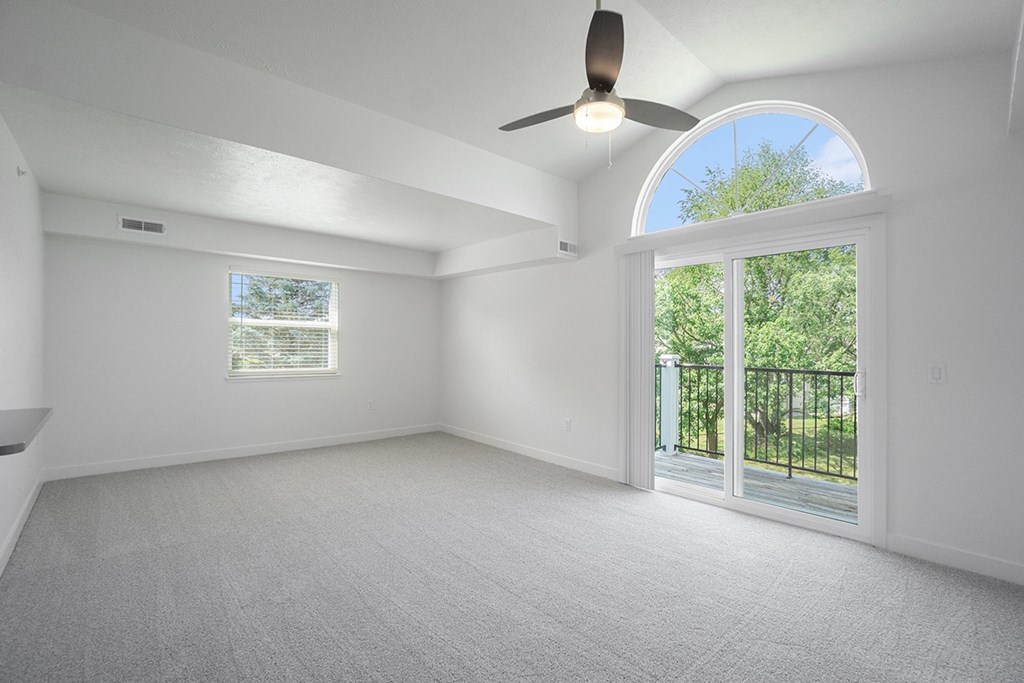 An end living room with a cathedral ceiling, ceiling fan and sliding glass doors leading to a balcony at Byron Lakes Apartments, Byron Center, Michigan