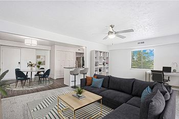 An enlarged living room with a grey couch, a coffee table, and a dining table with chairs at Byron Lakes Apartments in Byron Center, MI