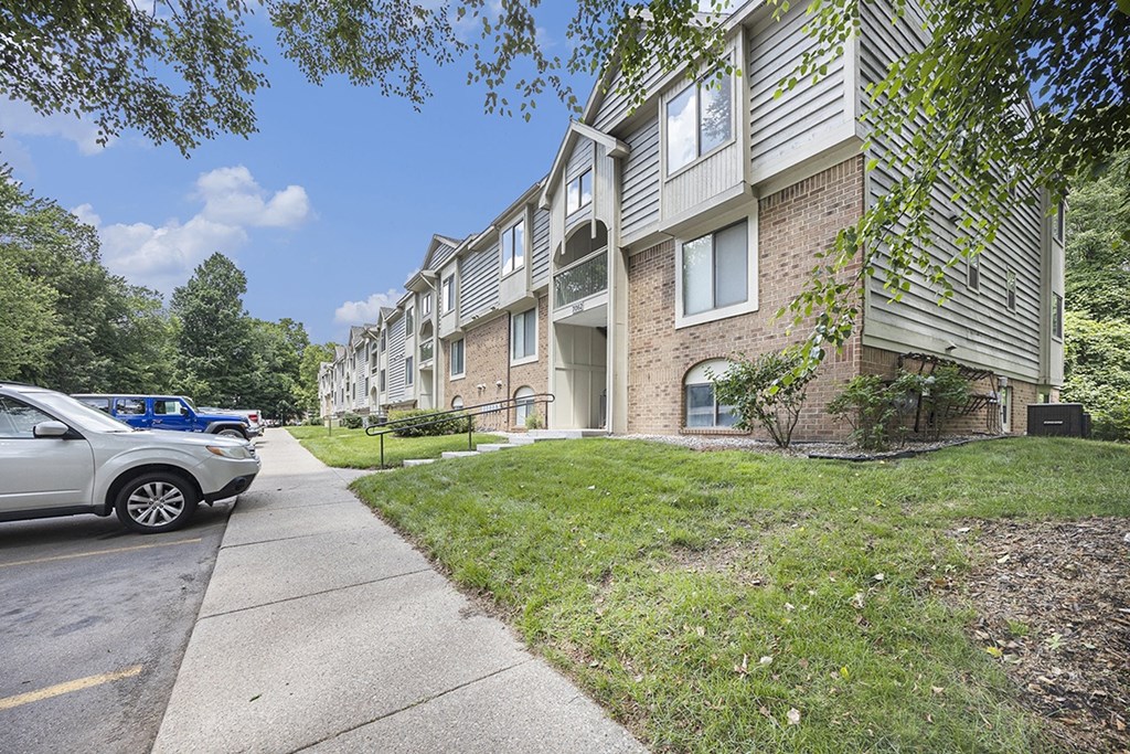 An exterior of an apartment building with a sidewalk and shade trees at Byron Lakes Apartments, Byron Center, Michigan