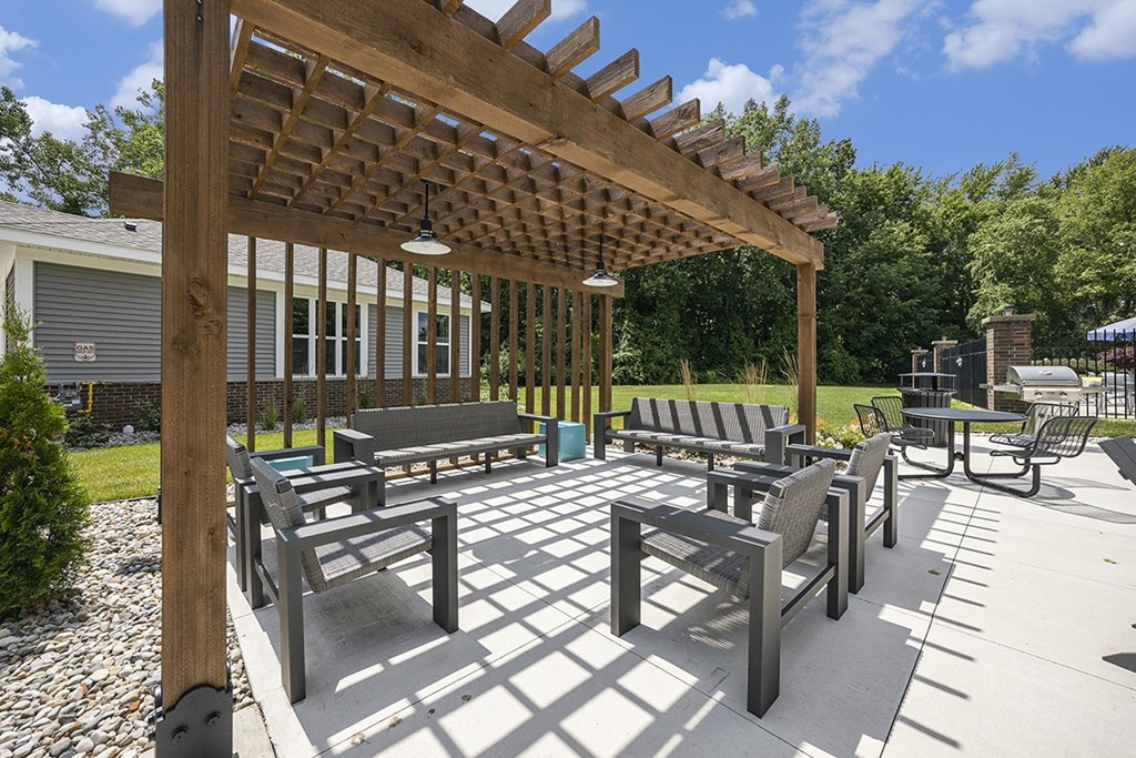 A wooden pergola with benches in a sunny outdoor area at Byron Lakes Apartments, Byron Center, MI