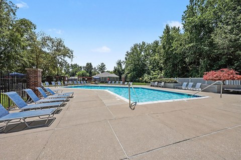 A pool surrounded by trees and chairs.