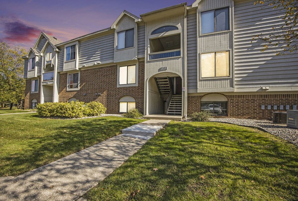 a sidewalk in front of an apartment building with beautiful landscaping at Byron Lakes Apartments, Byron Center