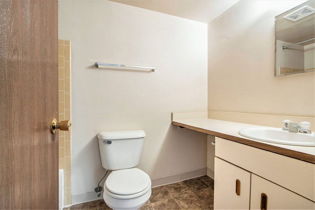 A bathroom with a toilet next to a sink and large vanity at Concord Place Apartments, Kalamazoo, MI, 49009
