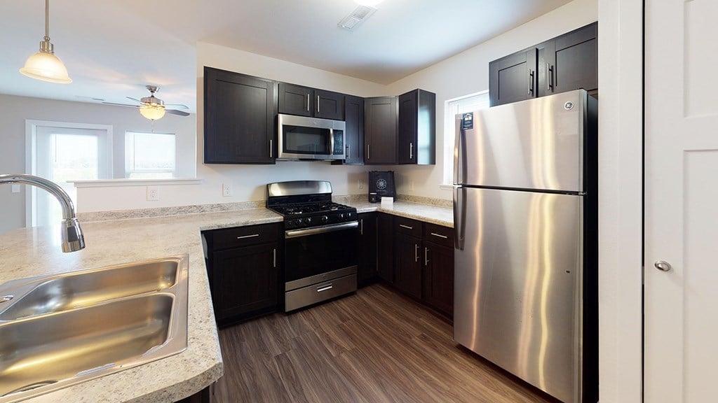 A modern kitchen with a stainless steel refrigerator, sink, and dark brown cabinets at Copper Creek Apartment Homes, Maize