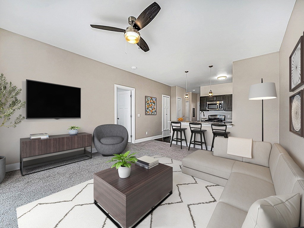 A living room with a grey armchair, sofa, wooden coffee table, and a television on the wall at Copper Creek Apartment Homes, Maize, Kansas
