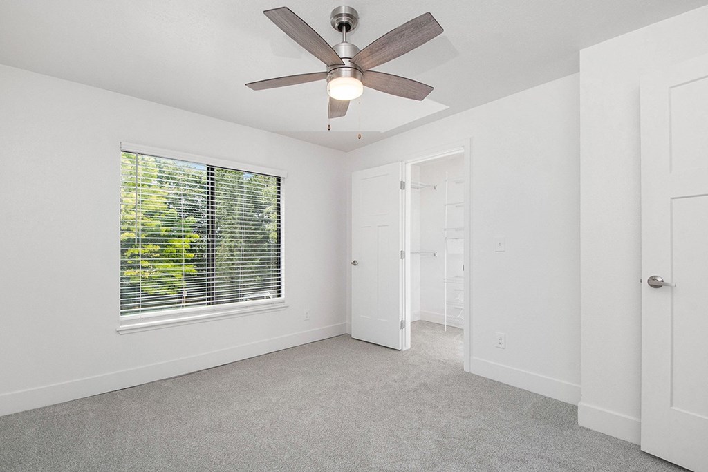 A bedroom with a ceiling fan and a window with blinds at The Crossings Apartments, Grand Rapids, Michigan