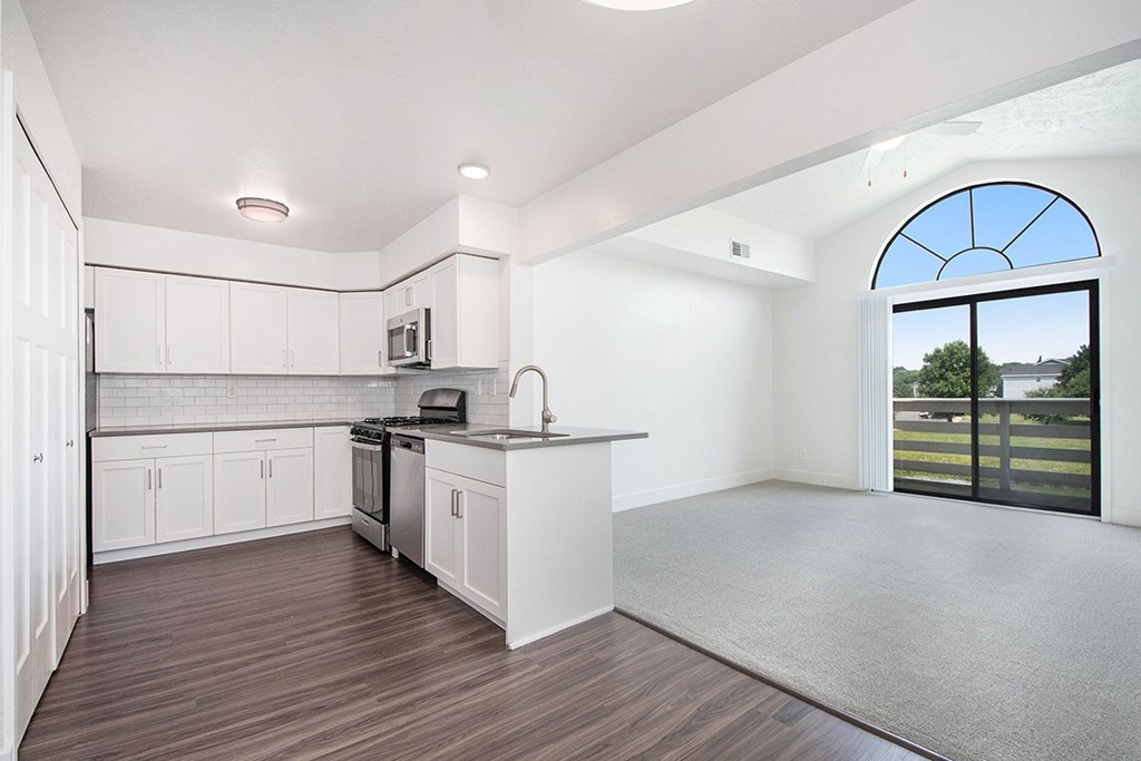 A kitchen with white cabinets and a living room with cathedral ceiling at The Crossings Apartments, Grand Rapids, MI, 49508