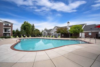 A large outdoor swimming pool surrounded by a concrete patio and buildings.