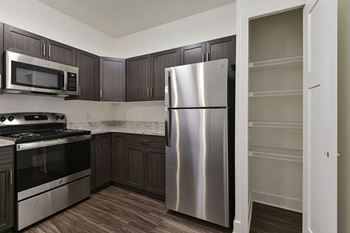 A kitchen with a stainless steel refrigerator and dark brown cabinets at Dodson Pointe Apartment Homes in Rogers, AR