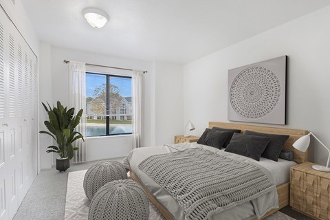 A bedroom with a large bed and a large window with a view at Dupont Lakes Apartments in Fort Wayne, IN