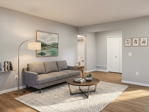 A living room with a grey couch, a round table, and a painting on the wall.