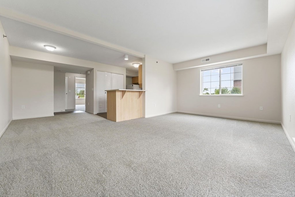 A large, empty living room with a carpeted floor and a window at Fieldstream Apartment Homes in IA 50023