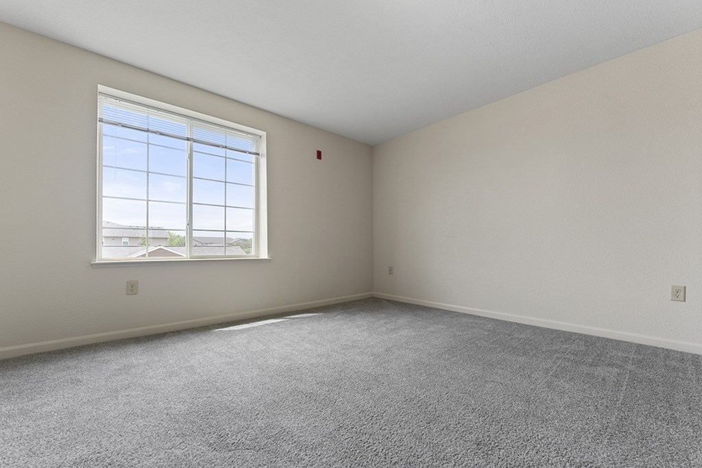 A bedroom with a large window and carpeted floor at Fieldstream Apartment Homes in IA 50023