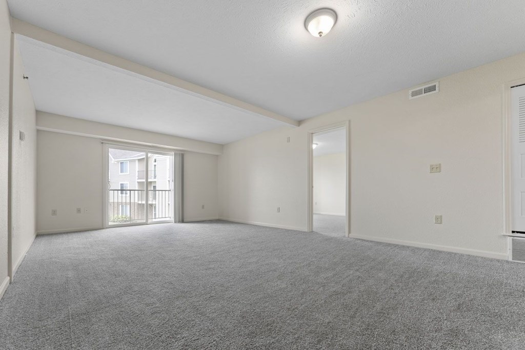 A spacious living room with a carpeted floor and a sliding glass door to a balcony at Fieldstream Apartment Homes in IA 50023