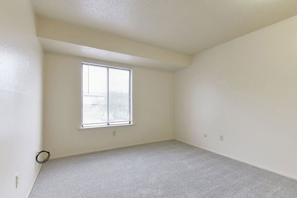 A bedroom with a large window and a carpeted floor at Granada Apartments, Jackson, 49202