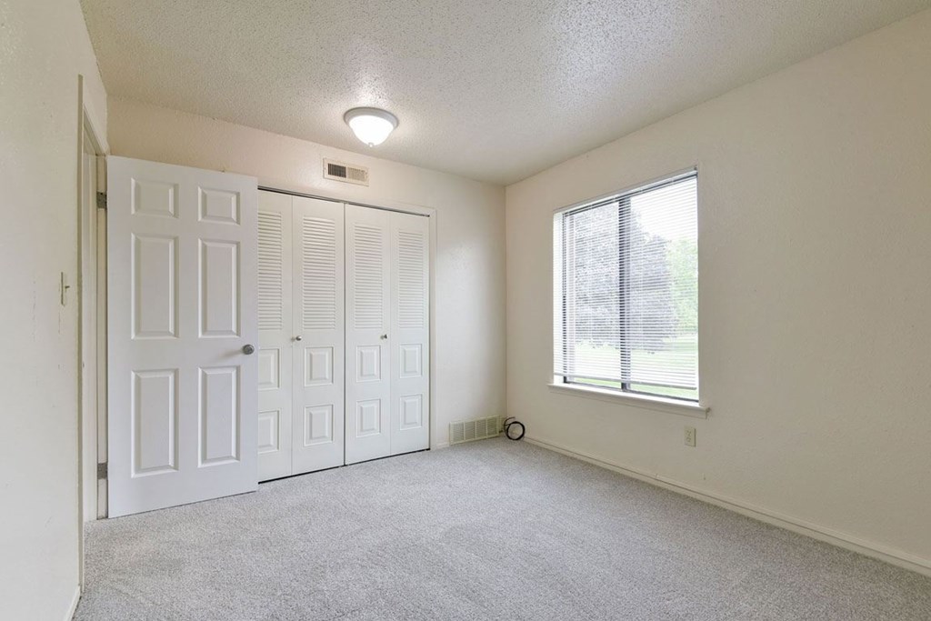A bedroom with a large window, closet and plush carpeting at Granada Apartments, Jackson, 49202